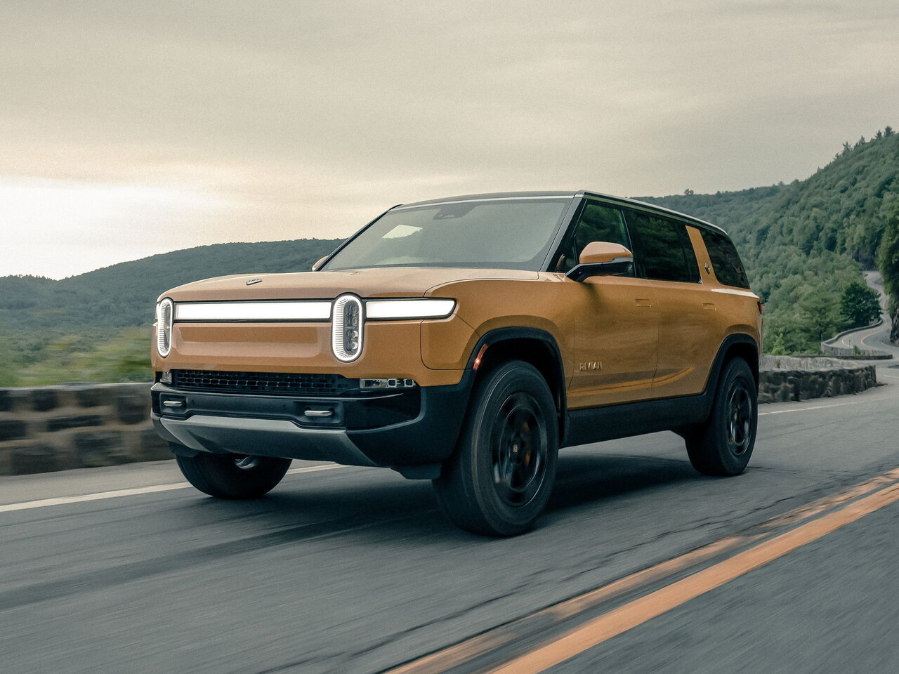 Rivian R1S 2022 года с фирменными овальными фарами и световой полосой на фоне горной дороги